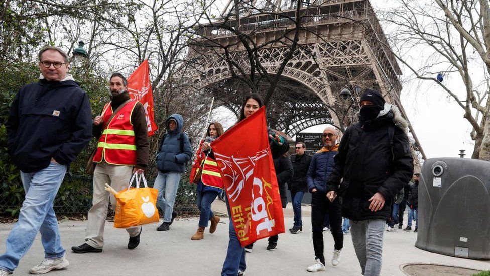 Protestors wearing the CGT union jacket walk past the Eiffel Tower